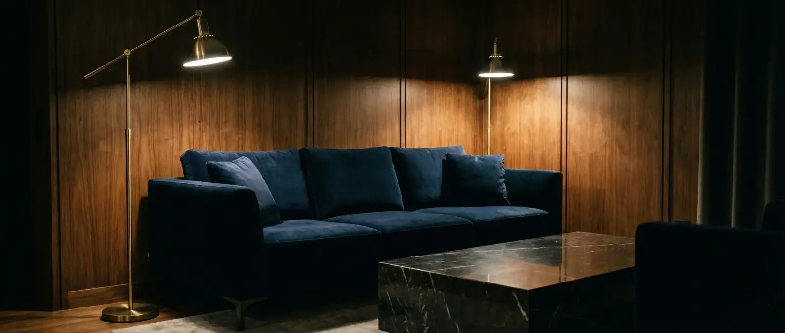 Elegancki salon z granatową welurową sofą, marmurowym stolikiem i mosiężnymi lampami